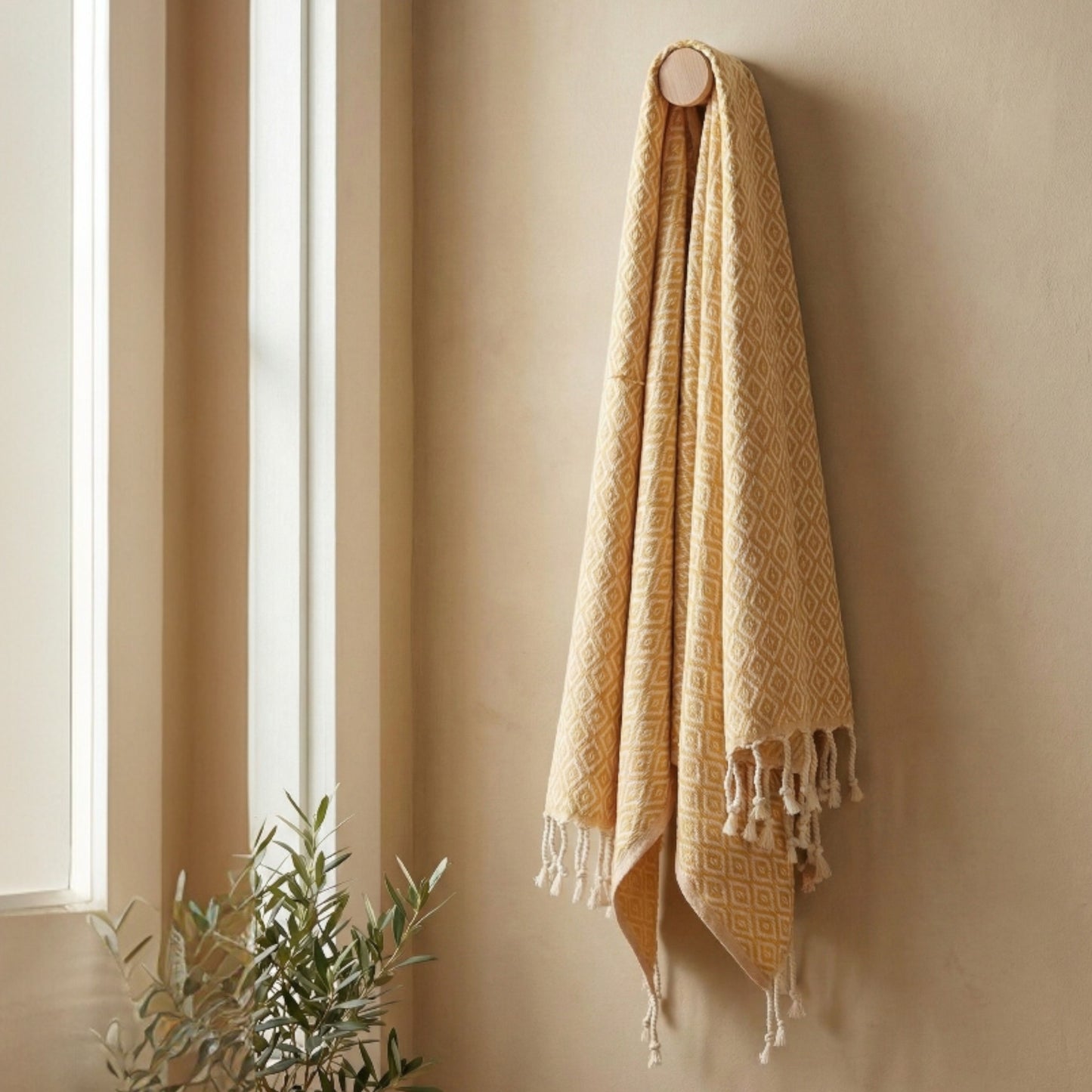 Beige Diamond Design Turkish Hand Towel Handwoven Natural Cotton Sustainable Anatolian Craft with tassels hanging on a beige wall next to a window.