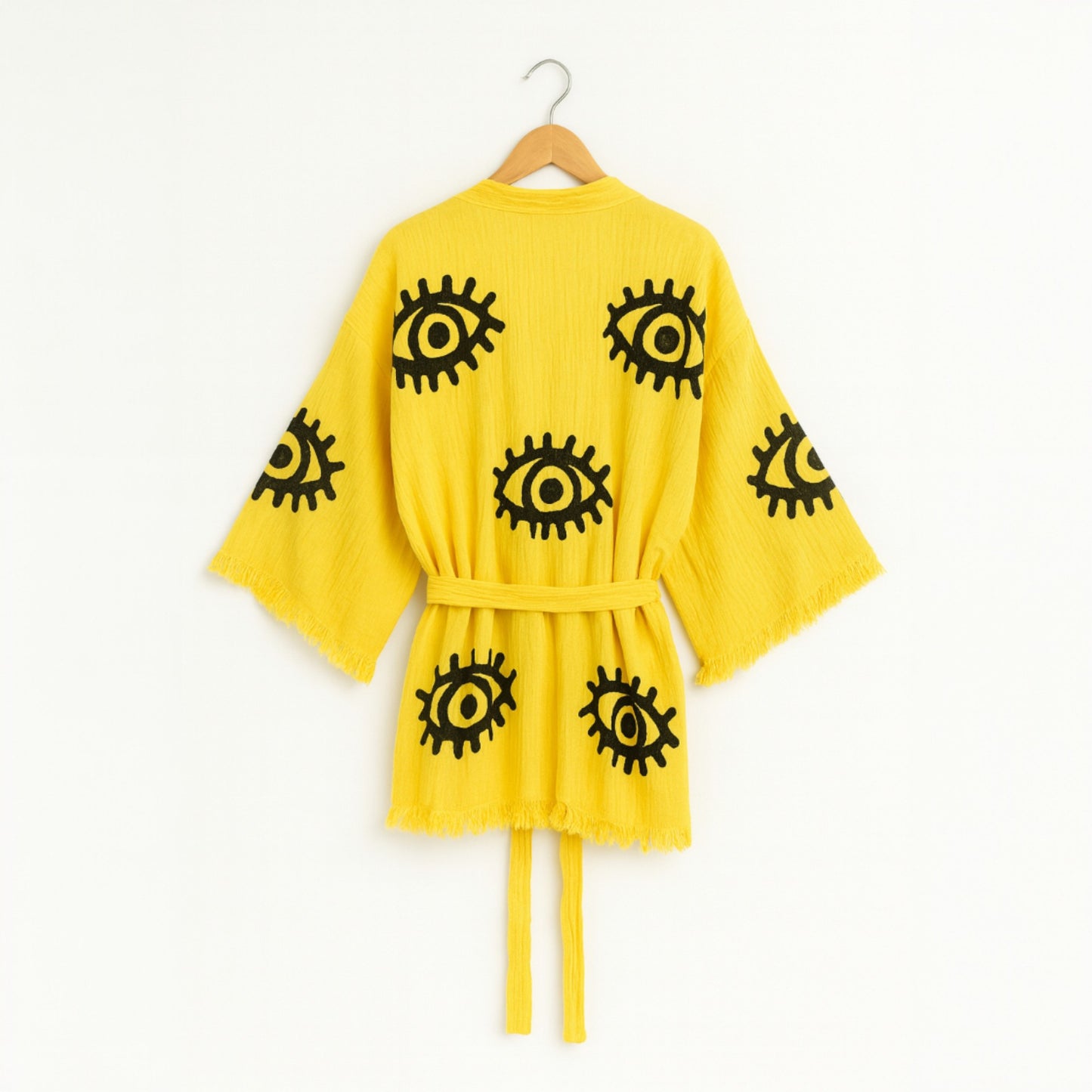 Yellow robe with black eye patterns on a hanger against a white background