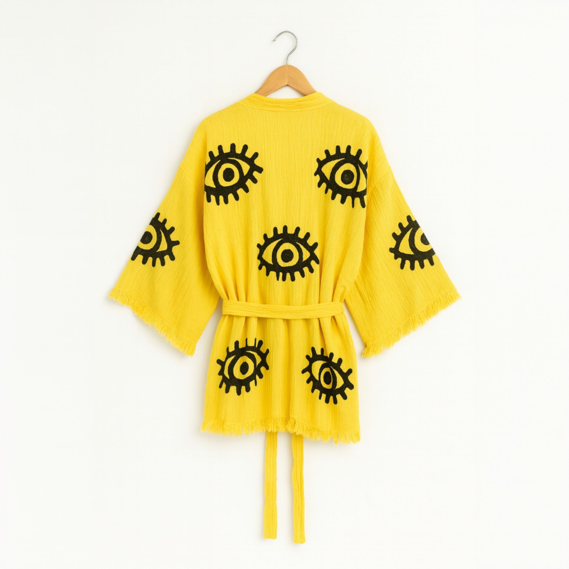 Yellow robe with black eye patterns on a hanger against a white background