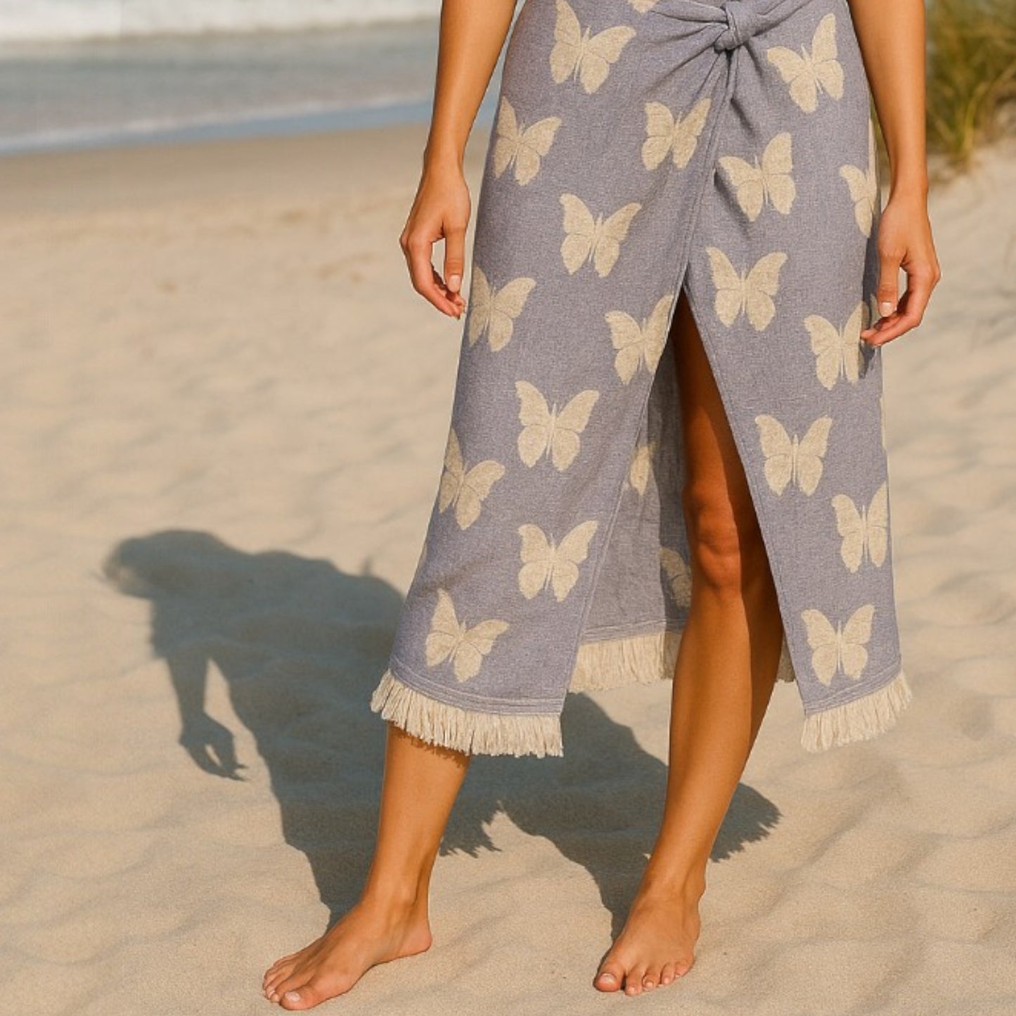 Person wearing a Handmade handwoven natural cotton muslin Turkish towel in blue with white butterfly design on a sandy beach.