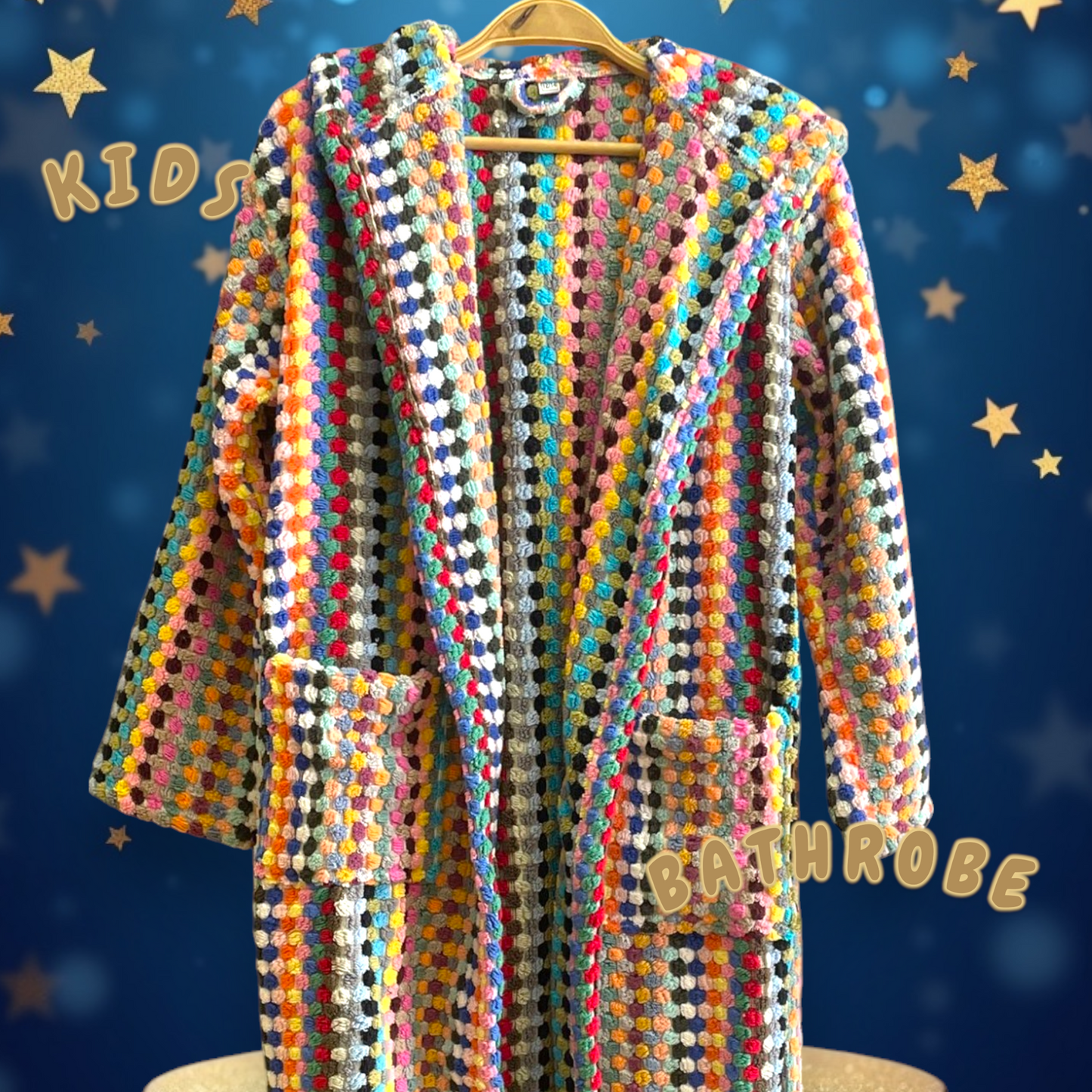 A colorful kids' bathrobe with geometric patterns and pompom details, displayed on a hanger with a blue background and star decorations.