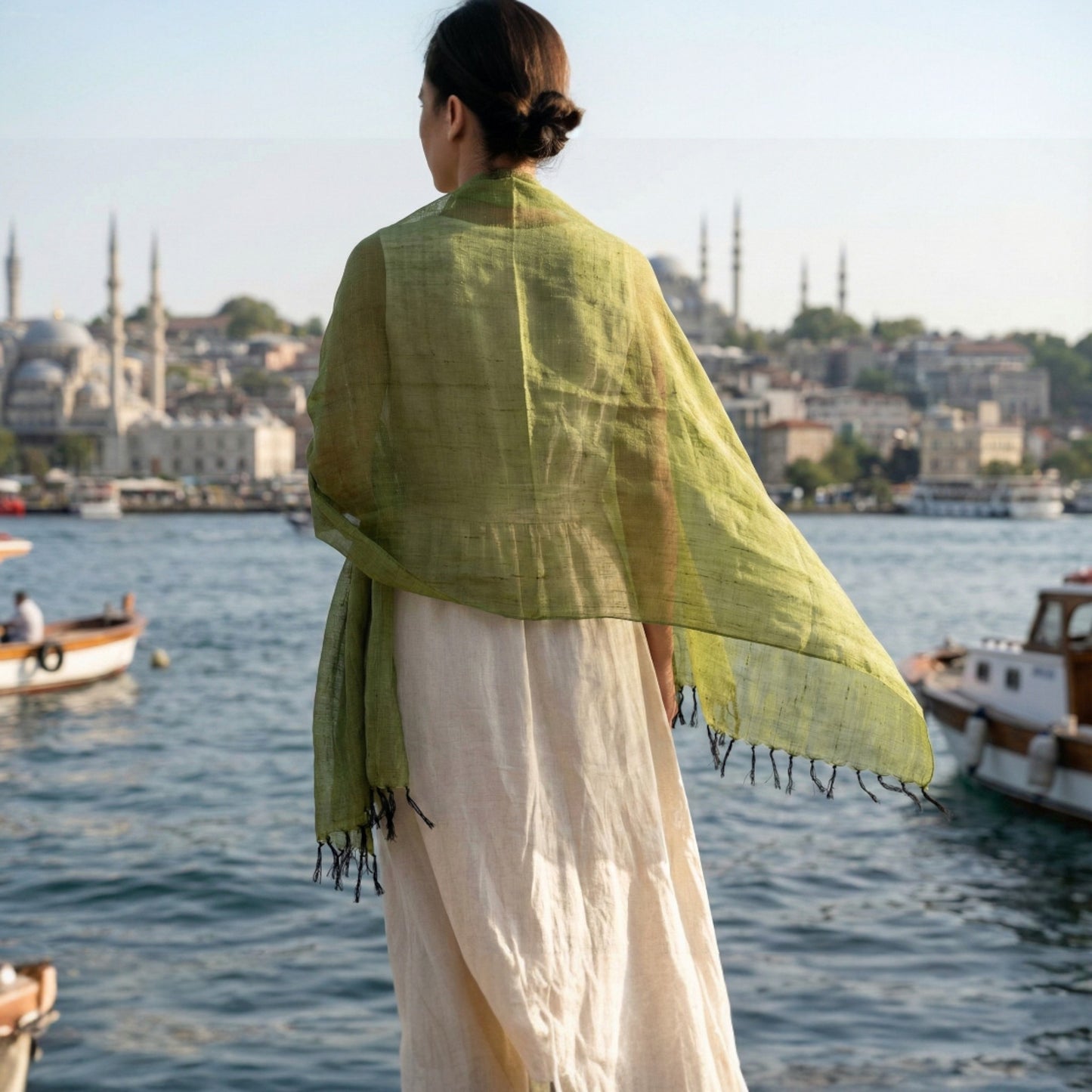 Person wearing a green Antakya Handwoven Silk Scarf overlooking a waterfront with boats and buildings in the background
