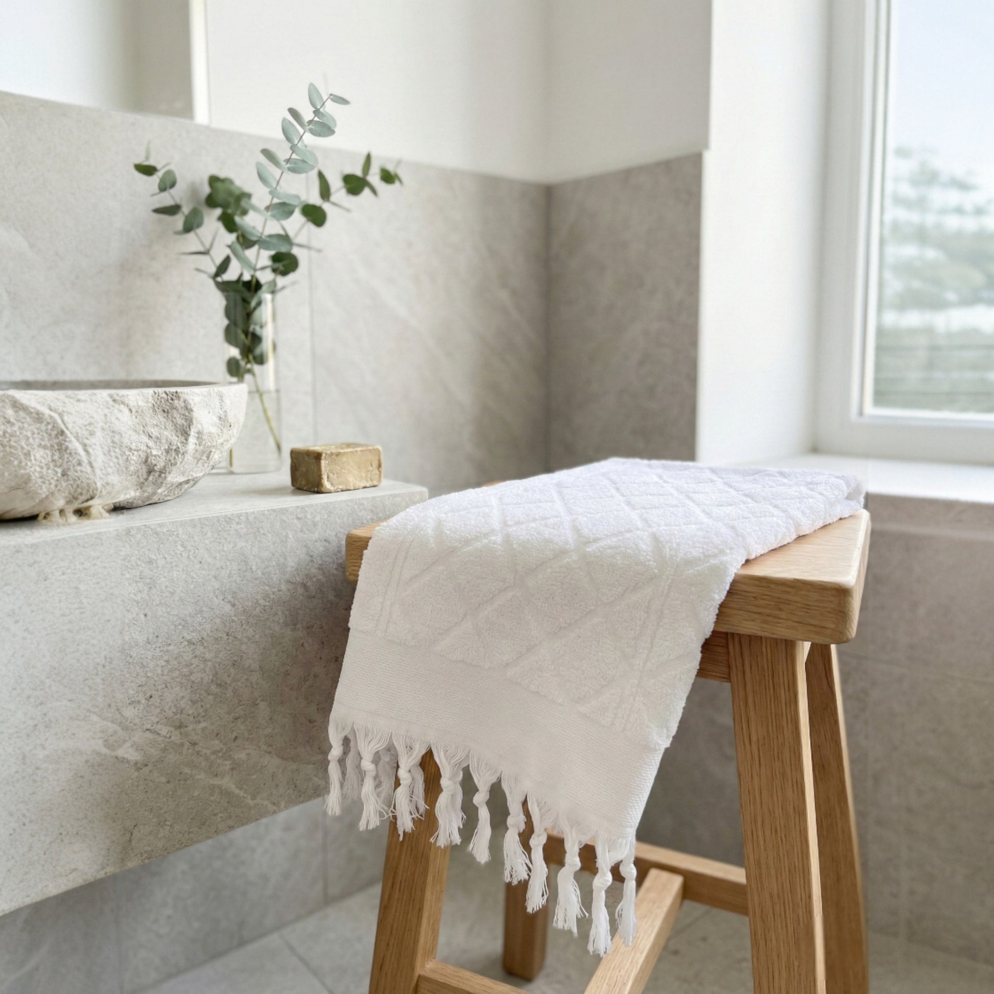 Hand-woven Baklava Design Turkish hand towel with traditional diamond pattern on a wooden stool in a bathroom setting.