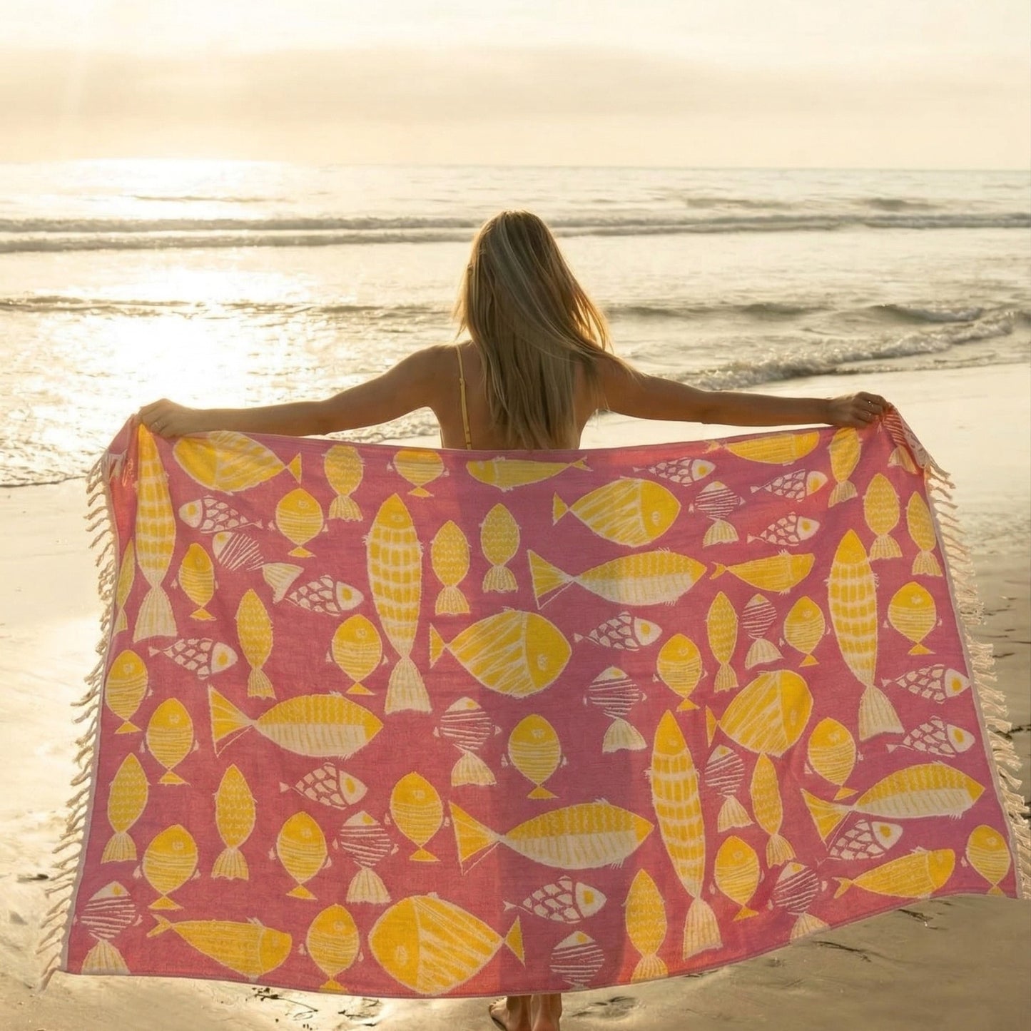 Woman holding a pinkFish Pattern 3-Layer Turkish Towel – Jacquard Woven Muslin Beach Towel on a beach at sunset