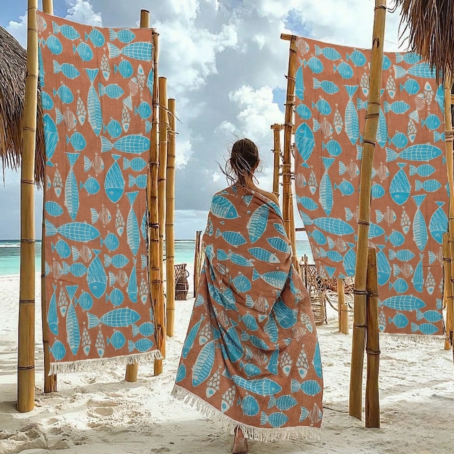 Woman wrapped in a Fish Pattern 3-Layer Turkish Towel – Jacquard Woven Muslin Beach Towel on a beach with decorative fish towels hanging on bamboo stands.