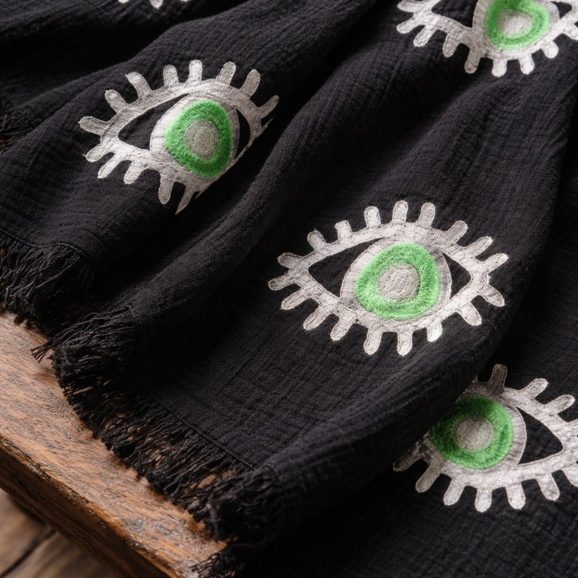 Black fabric with green and white embroidered eye designs on a wooden surface