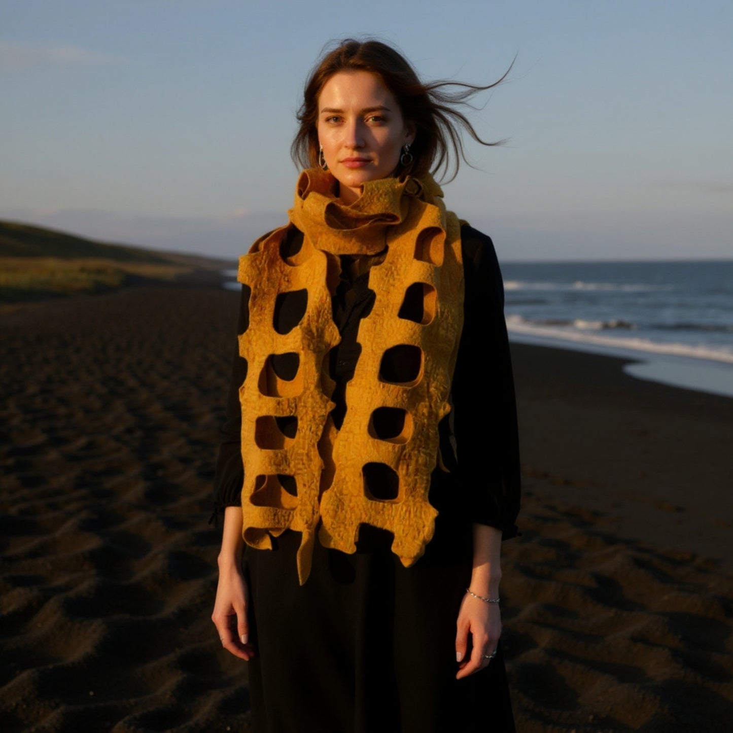 Woman wearing a Handmade felted wool shawl/scarf in golden yellow, with cut-out design, soft textured fabric, 35x95 cm on a beach at sunset