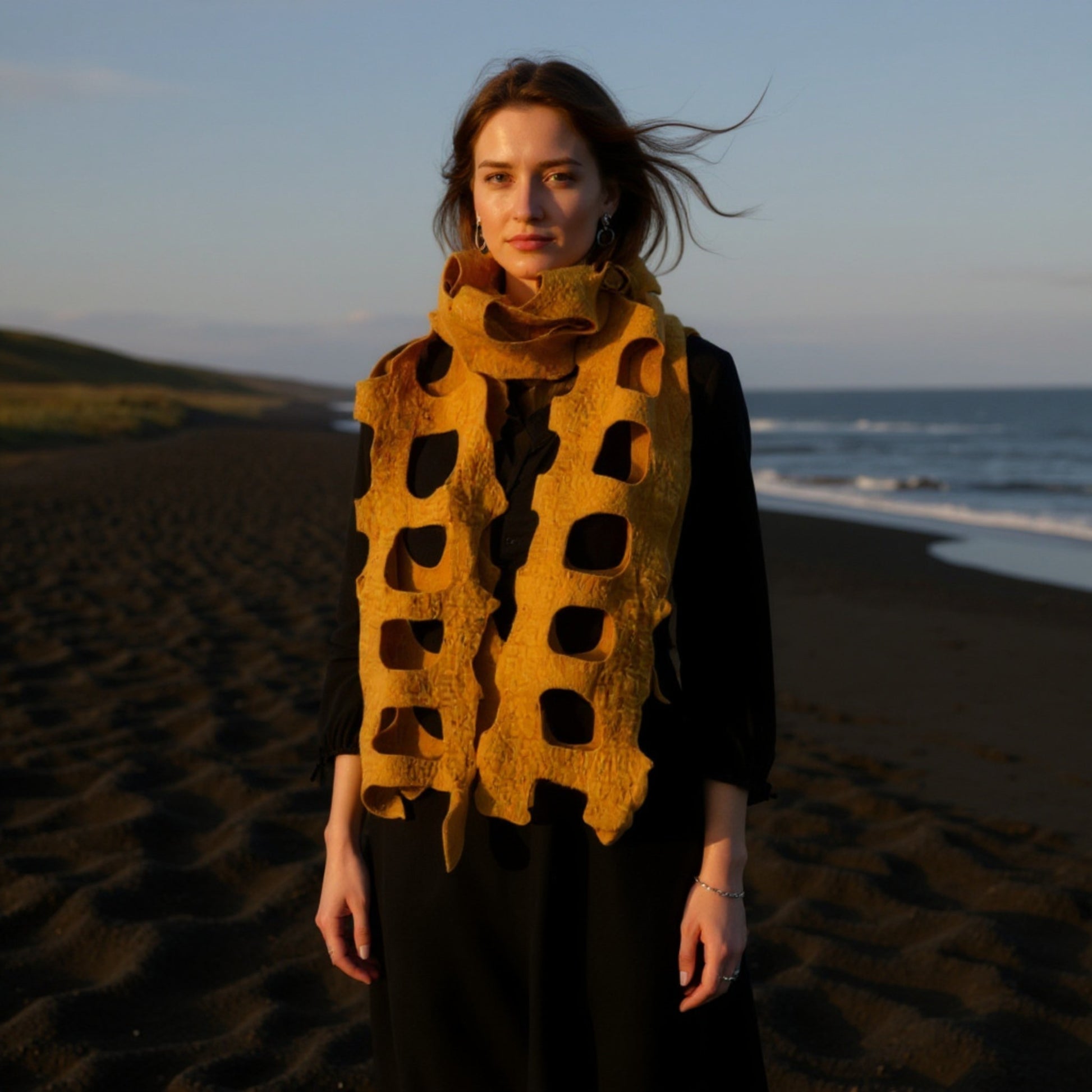 Woman wearing a Handmade felted wool shawl/scarf in golden yellow, with cut-out design, soft textured fabric, 35x95 cm on a beach at sunset