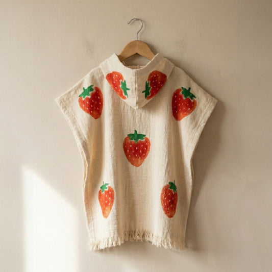 Beige sleeveless Handmade Natural Cotton Kids Poncho – Strawberry Design on a wooden hanger against a beige wall.