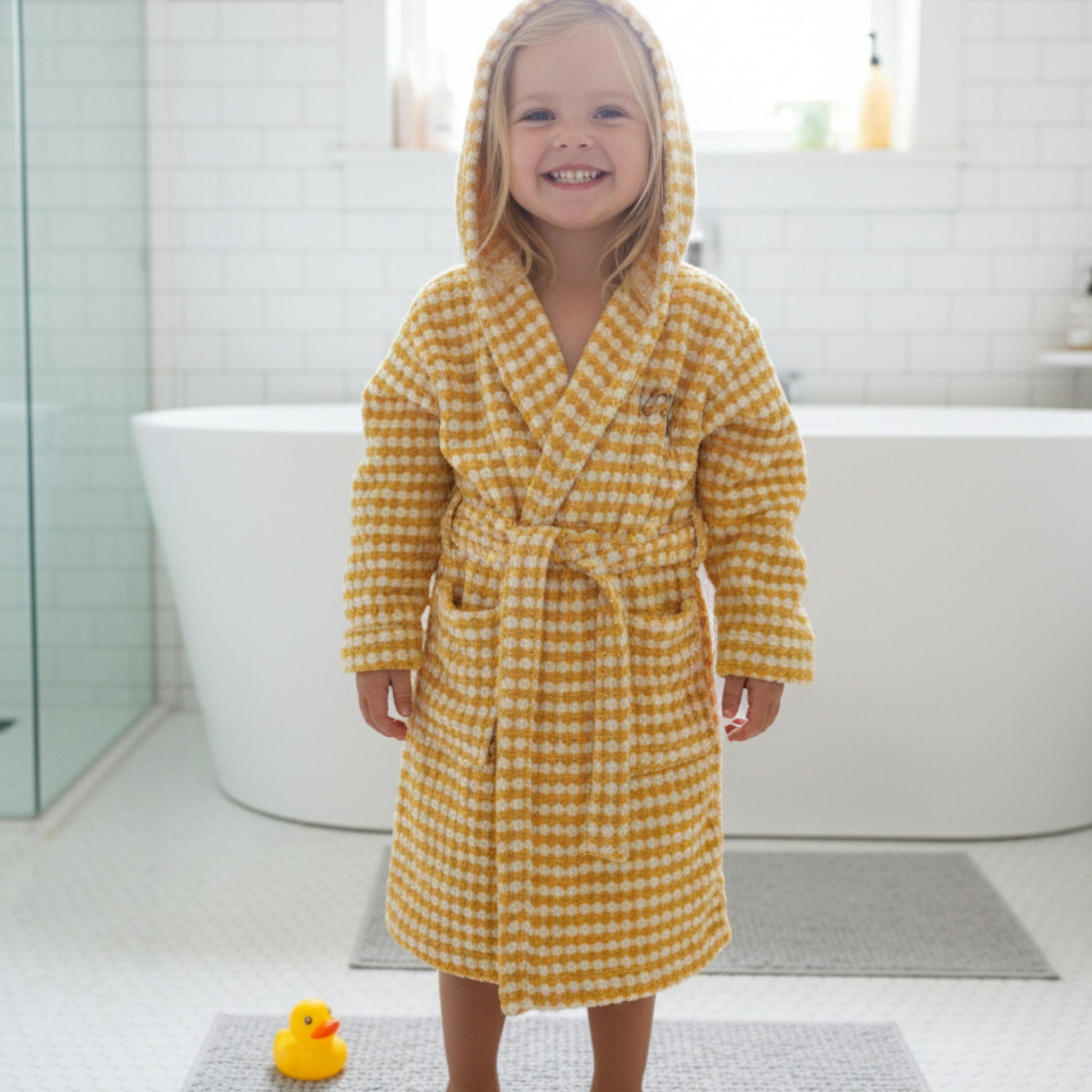 Child wearing Handwoven Natural Turkish Cotton Terry Kids Bathrobe – PomPom Design Golden Yellow Hoodedrobe in a bathroom