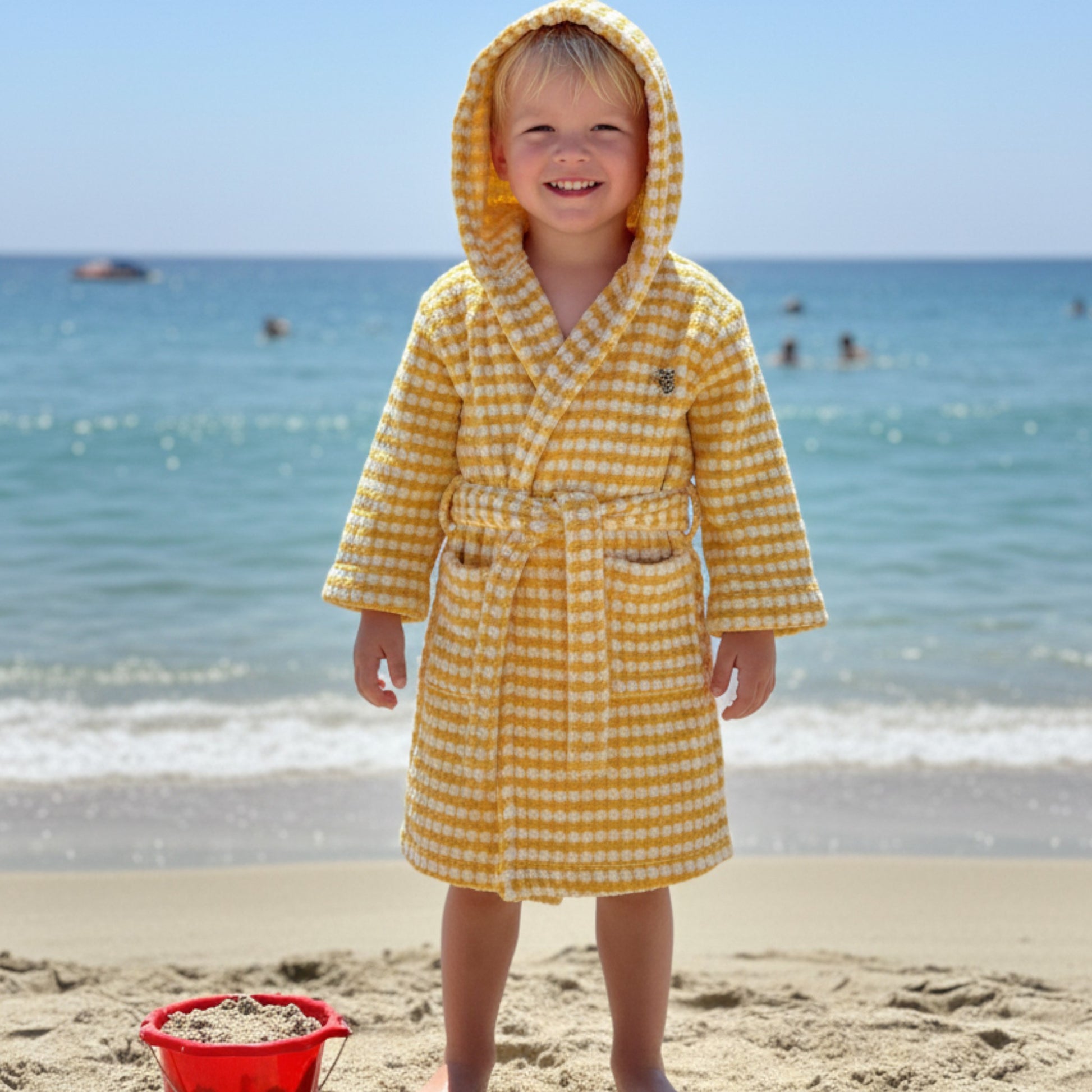 Child in a yellow checkered robe standing on a beach with ocean in the background