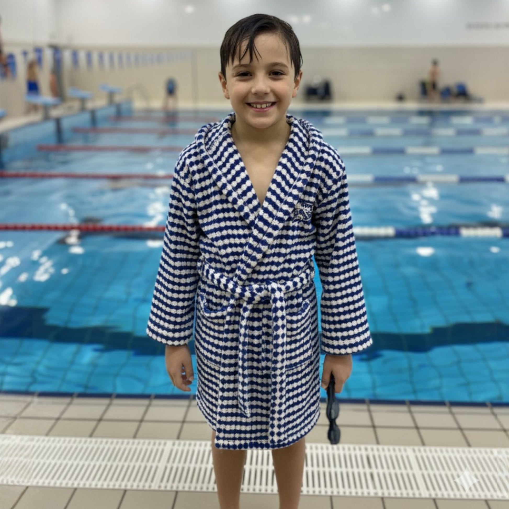 Child in a blue and white checkered robe standing by a pool