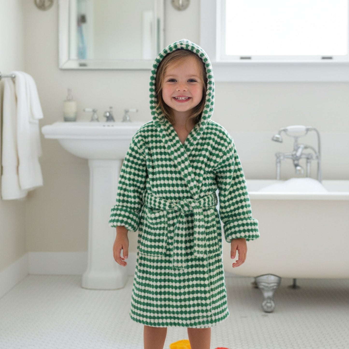 Child wearing a green and white checkered robe in a bathroom.
