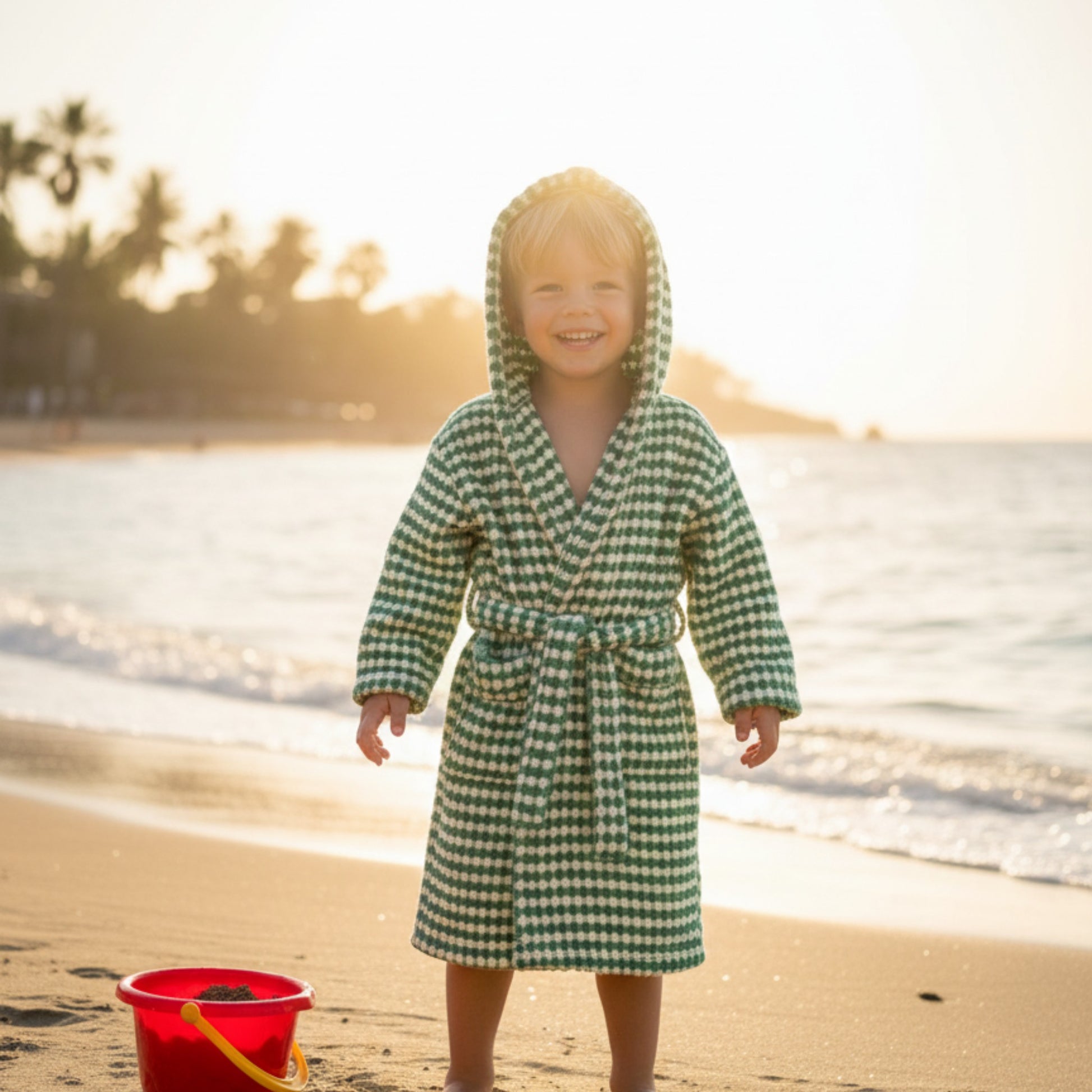 Child in a green checkered robe standing on a beach with sunset in the background