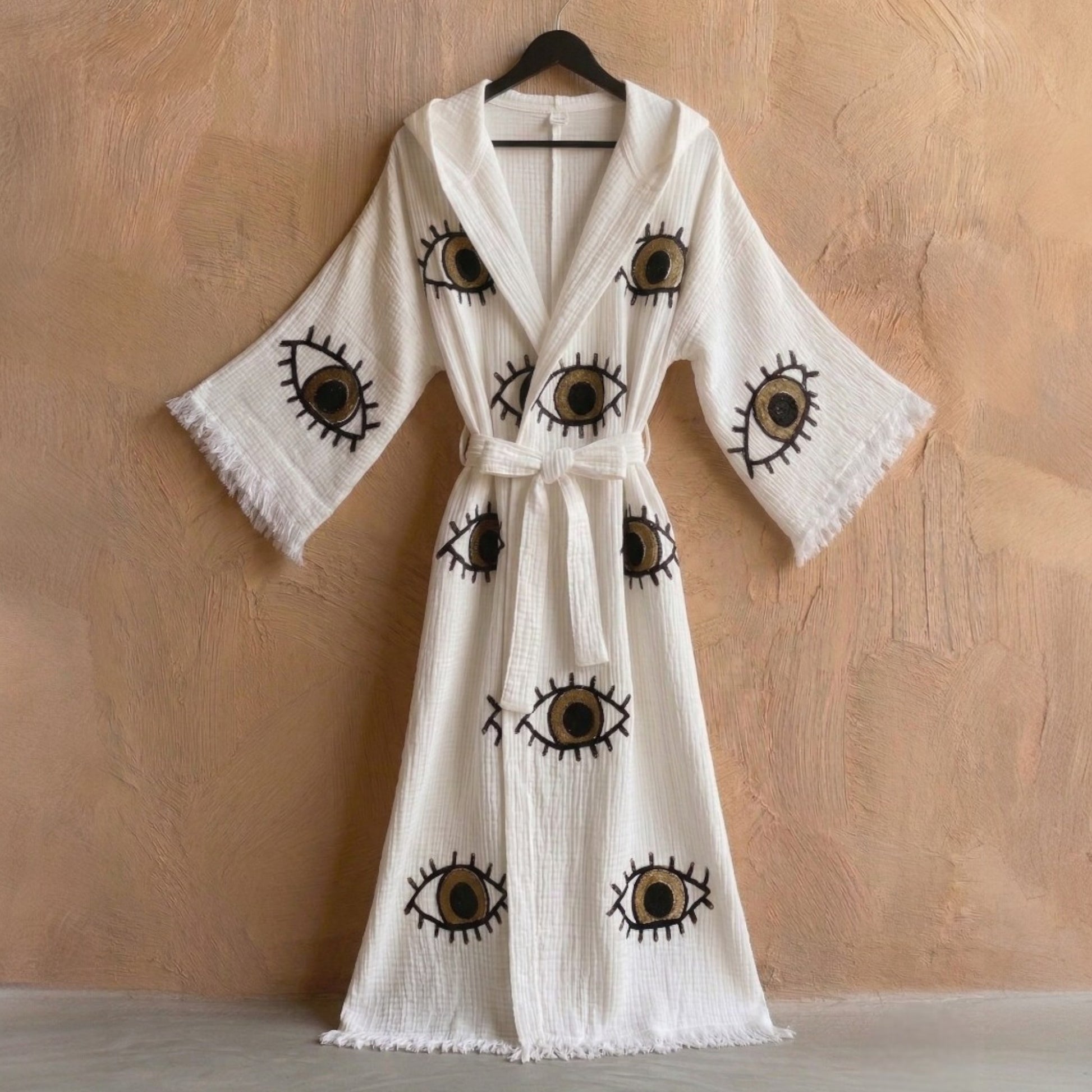 Hooded Turkish Towel Kimono Robe – Handwoven Muslin Cotton, Brown Evil Eye Design on a hanger against a beige wall