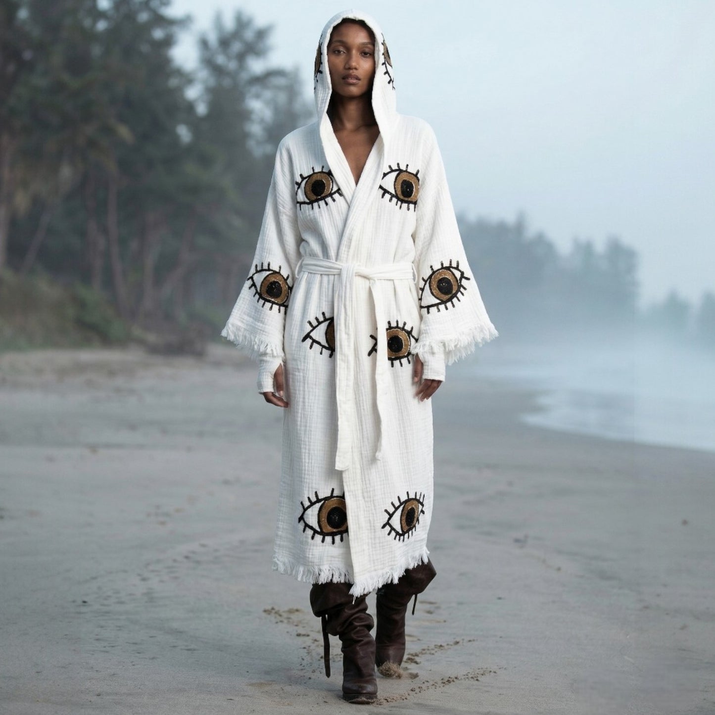 Person wearing a long,Hooded Turkish Towel Kimono Robe – Handwoven Muslin Cotton, Brown Evil Eye Design on a beach.
