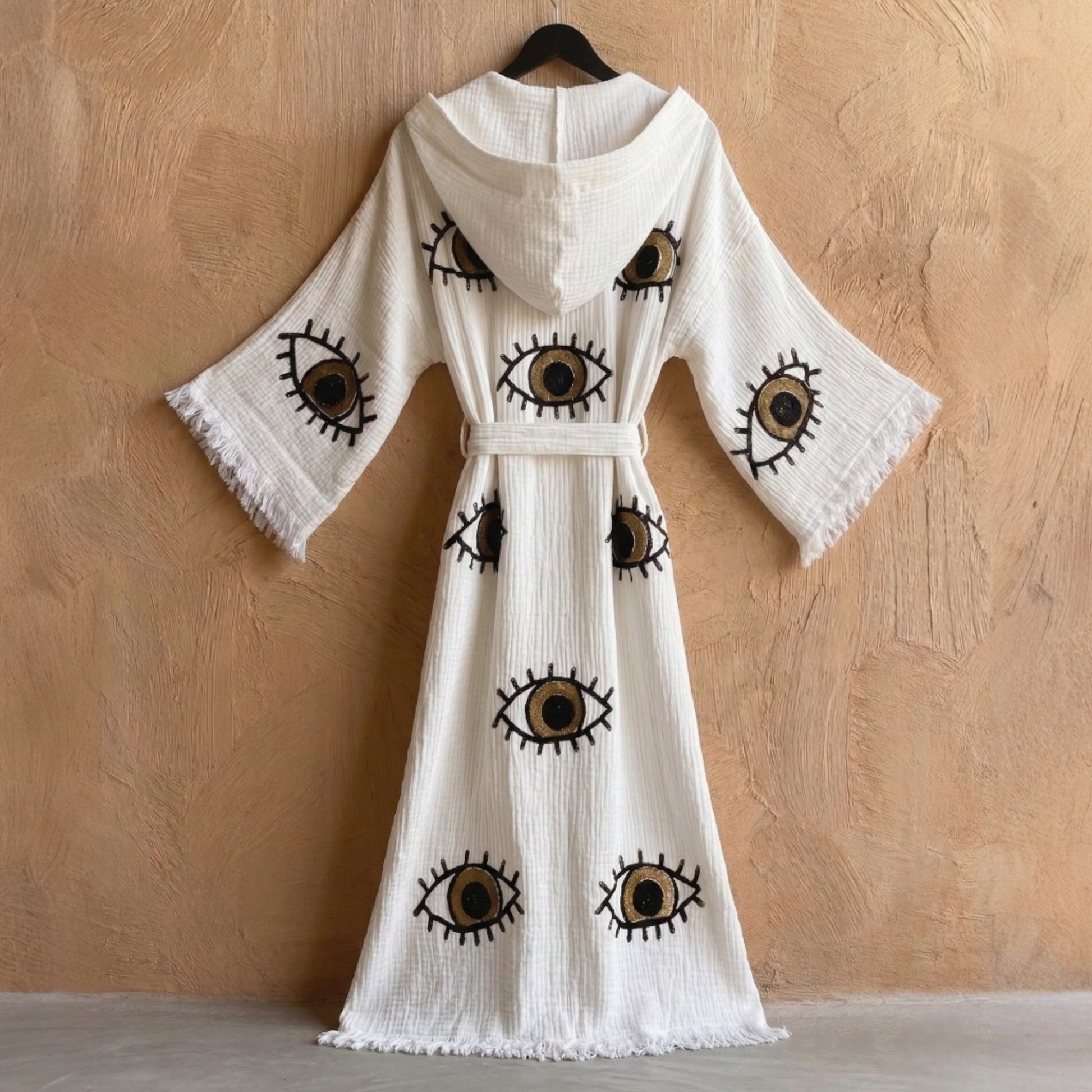 Hooded Turkish Towel Kimono Robe – Handwoven Muslin Cotton, Brown Evil Eye Design hanging against a beige wall