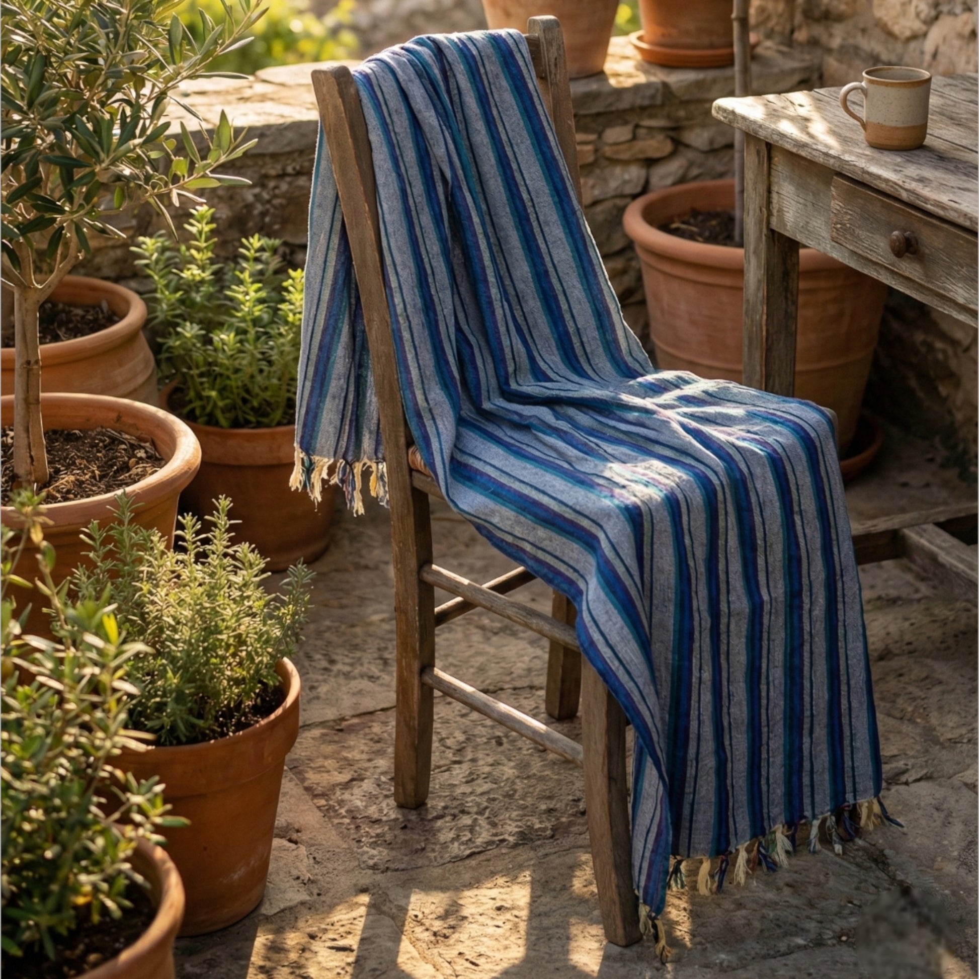 Blue striped Hand-woven linen Turkish towel pestemal draped over a wooden chair in an outdoor setting with potted plants.