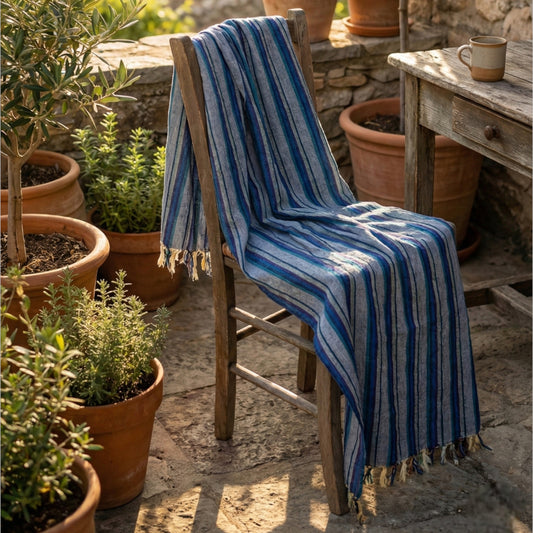 Blue striped Hand-woven linen Turkish towel pestemal draped over a wooden chair in an outdoor setting with potted plants.