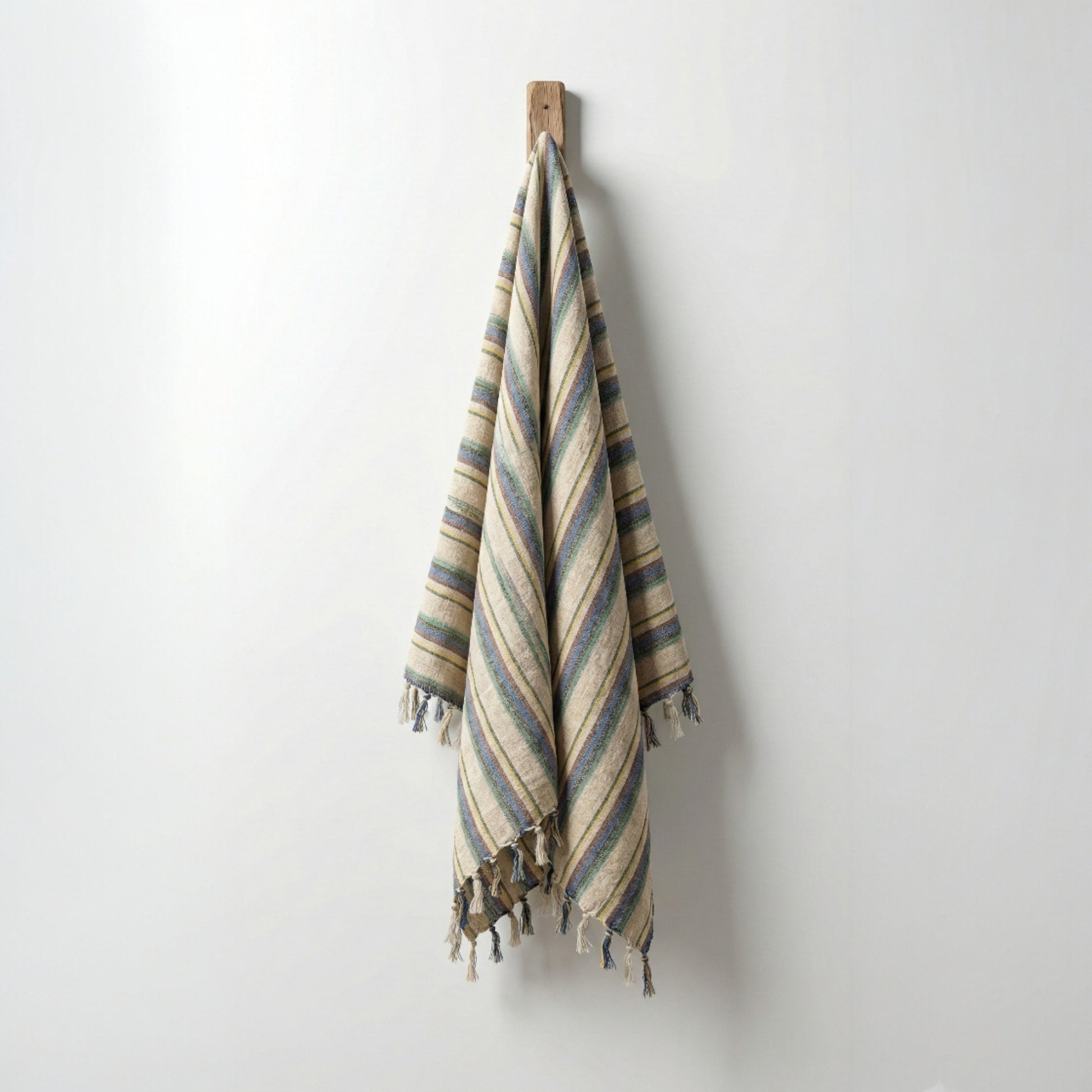 Striped Hand-woven linen Turkish towel pestemal  with tassels hanging on a wooden hook against a white wall