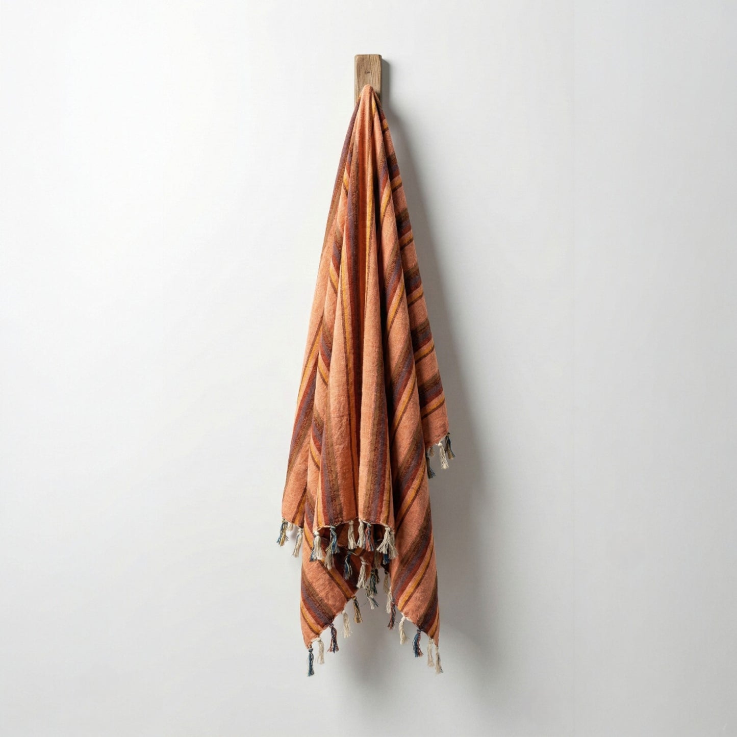Striped Hand-woven linen Turkish towel pestemal with tassels hanging on a wooden hook against a white wall