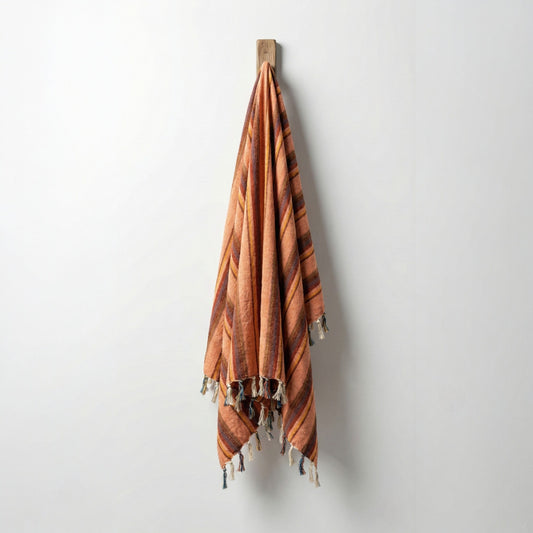 Striped Hand-woven linen Turkish towel pestemal with tassels hanging on a wooden hook against a white wall