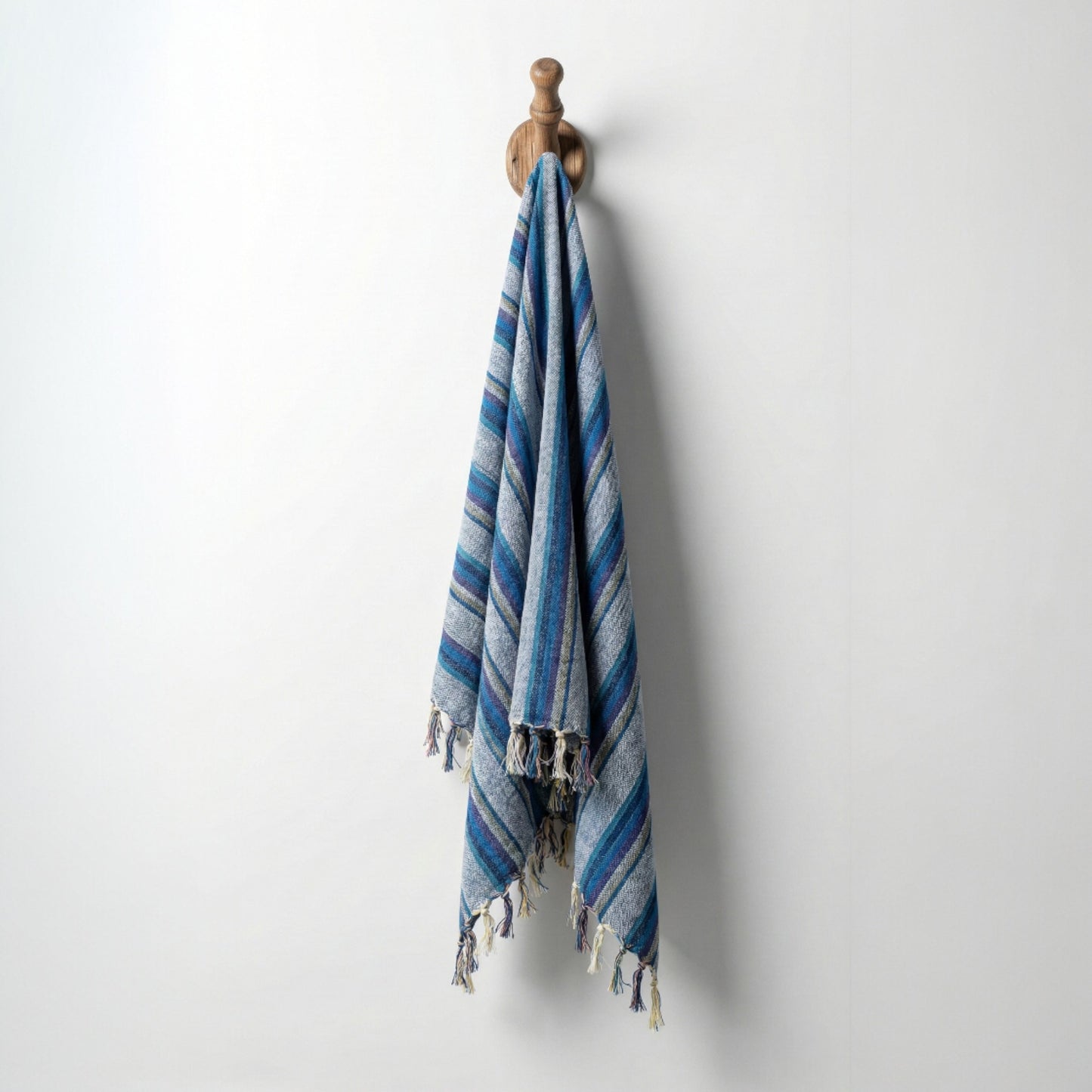 Blue striped Hand-woven linen Turkish towel pestemal with tassels hanging on a wooden hook against a white background