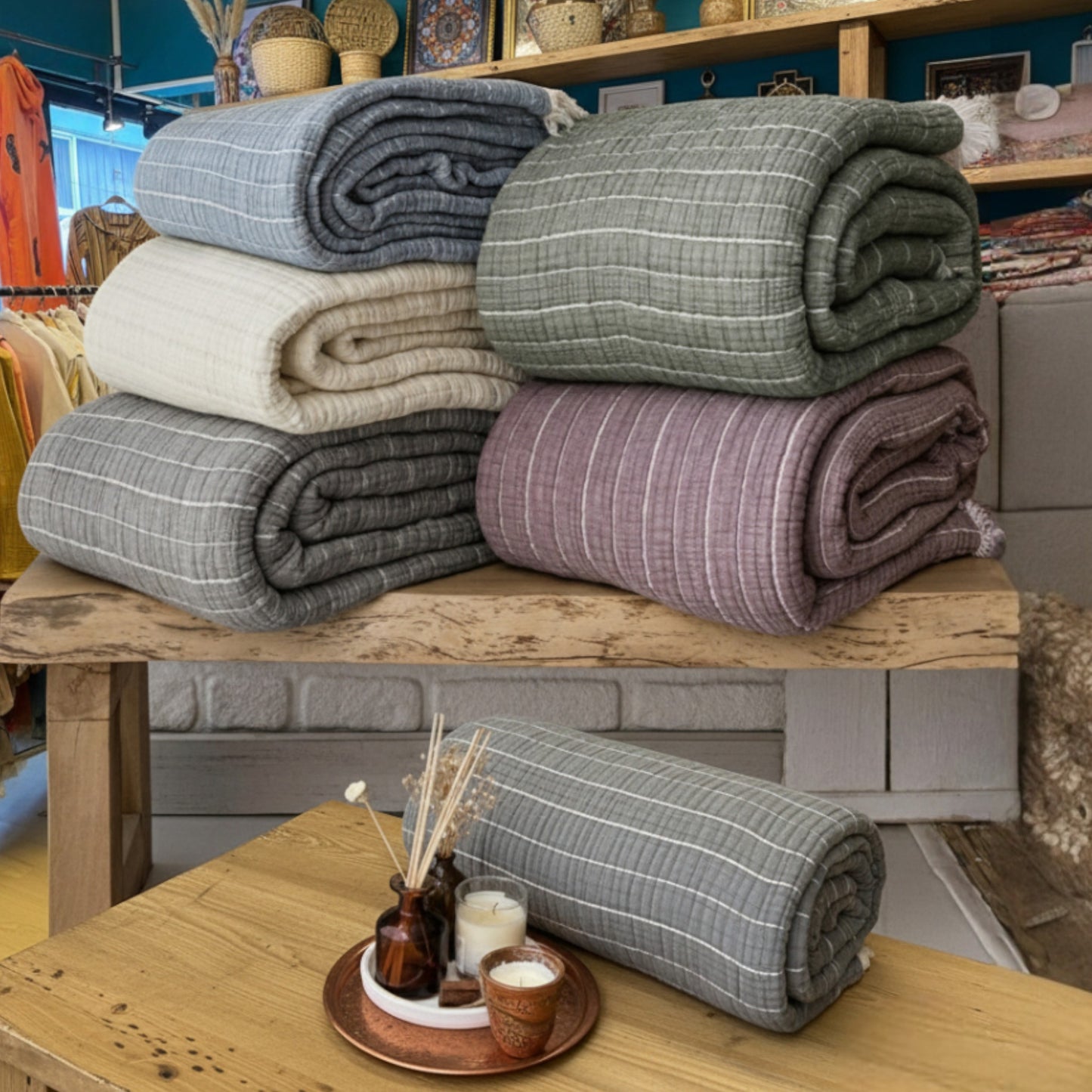 Stack of folded Muslin Ribbed Soft Quilt – 7 Layers of Dreamlike Comfort in various colors on a wooden surface with a blurred store interior.