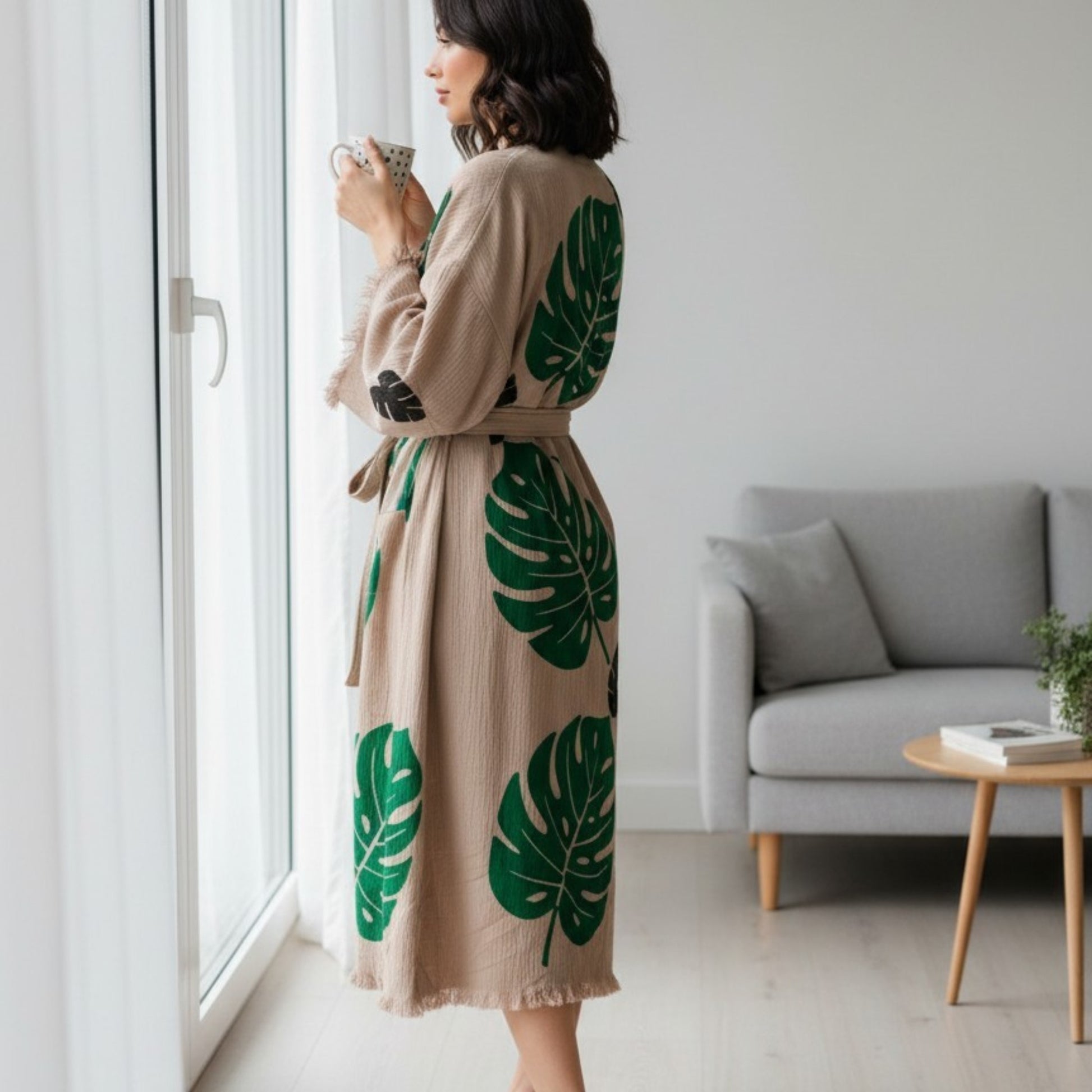 Woman in a beige Turkish Towel Kimono Robe – Hand Block Printed Natural Cotton Kimono | Evil Eye Kimono Robe Collection standing by a window in a modern living room.