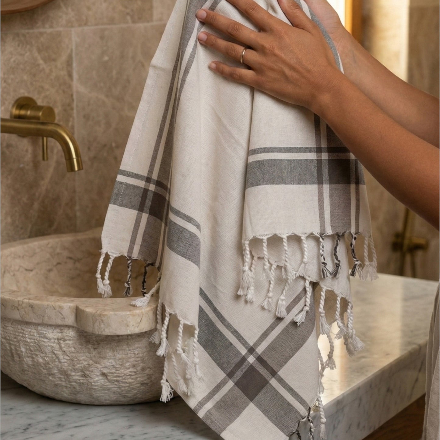 Person holding a plaid Traditional Turkish Peşkir — Hand-Woven, Hand-Knotted, Natural Cotton in a bathroom setting