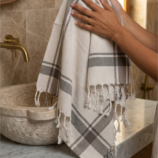 Person holding a plaid Traditional Turkish Peşkir — Hand-Woven, Hand-Knotted, Natural Cotton in a bathroom setting