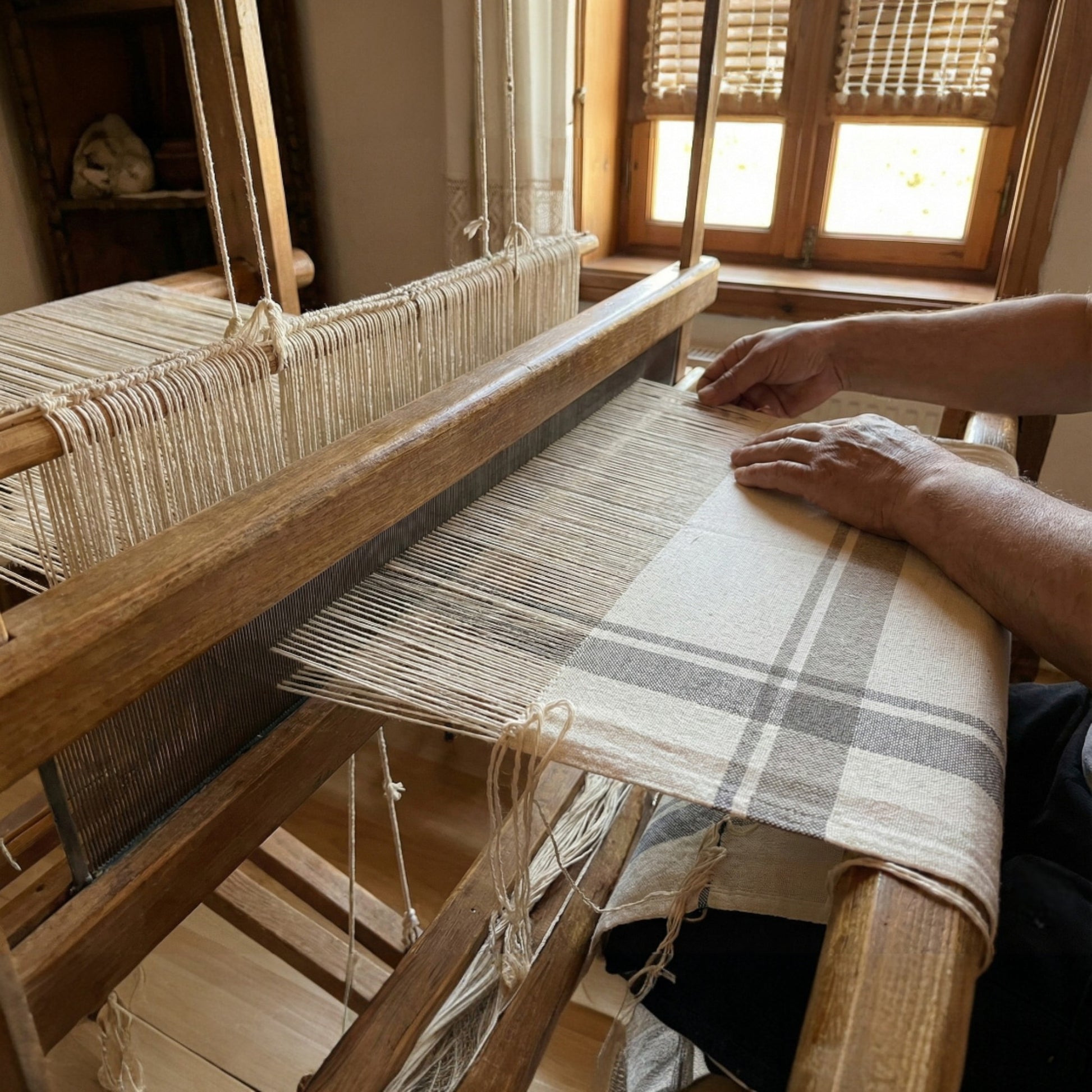 Person weaving Traditional Turkish Peşkir  Hand-Woven, Hand-Knotted, Natural Cotton on a wooden loom with fabric in a room with windows.