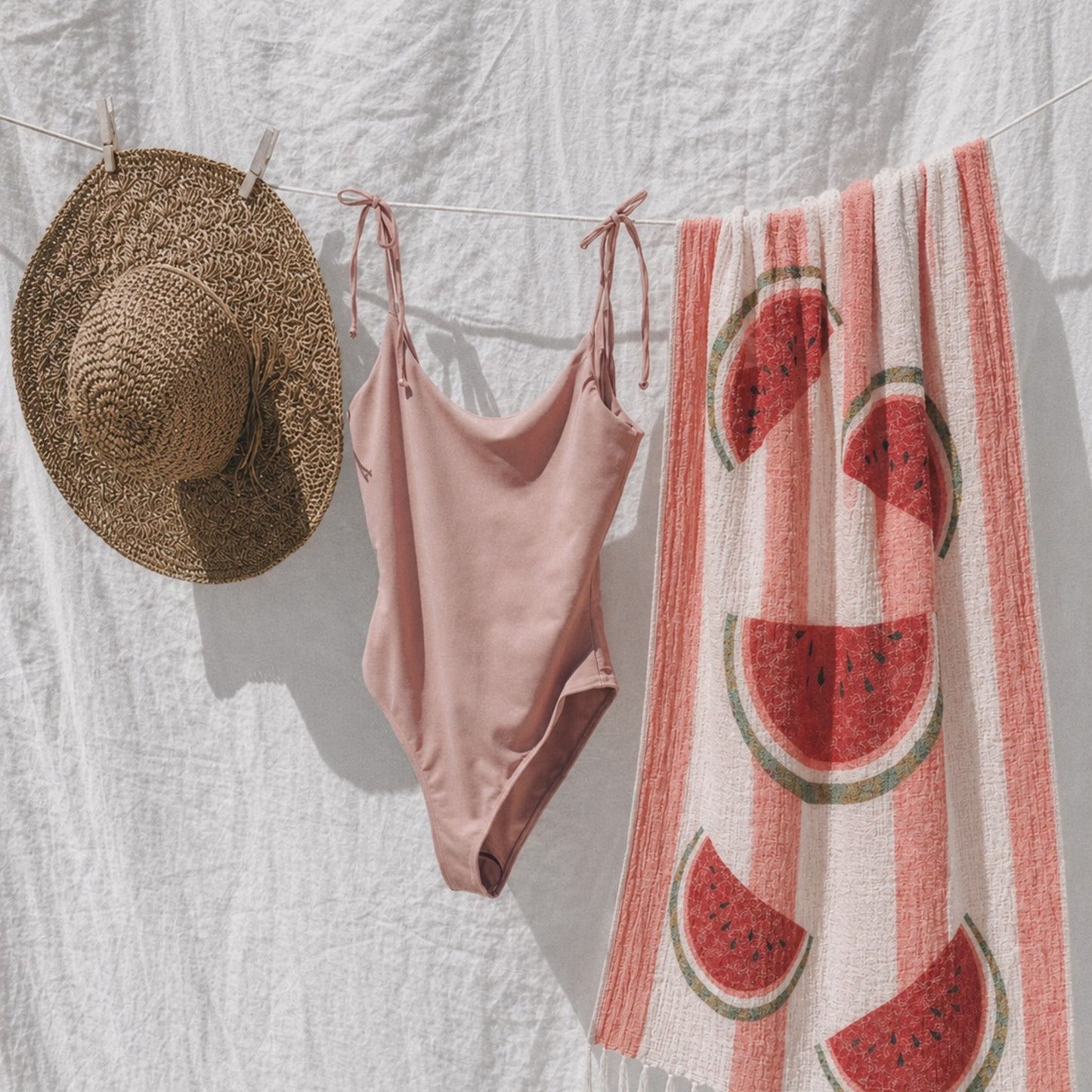 Reversible Watermelon Turkish Towel hanging on a clothesline with a straw hat and beach bag, made from 100% premium Turkish cotton muslin.
