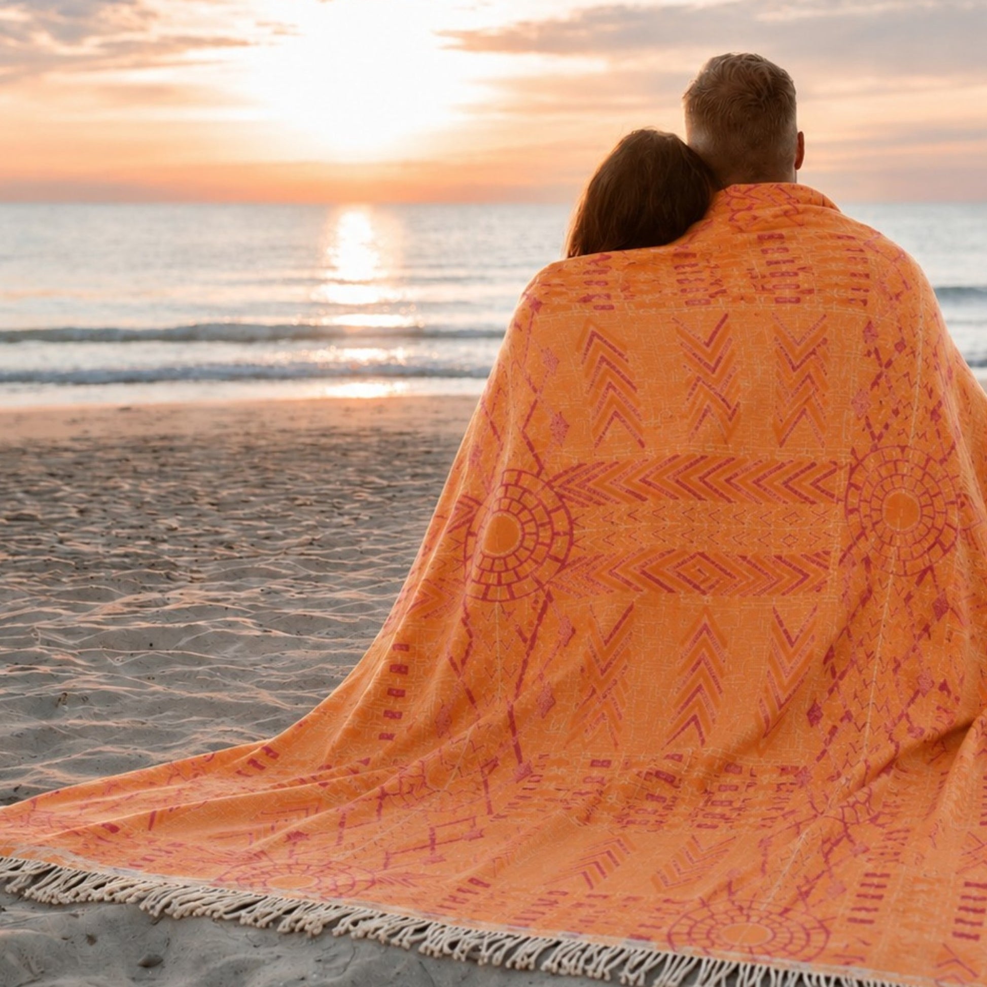 Couple wrapped in the Kilim Heritage reversible Turkish cotton muslin throw blanket on the beach at sunset, featuring a jacquard woven ethnic pattern.